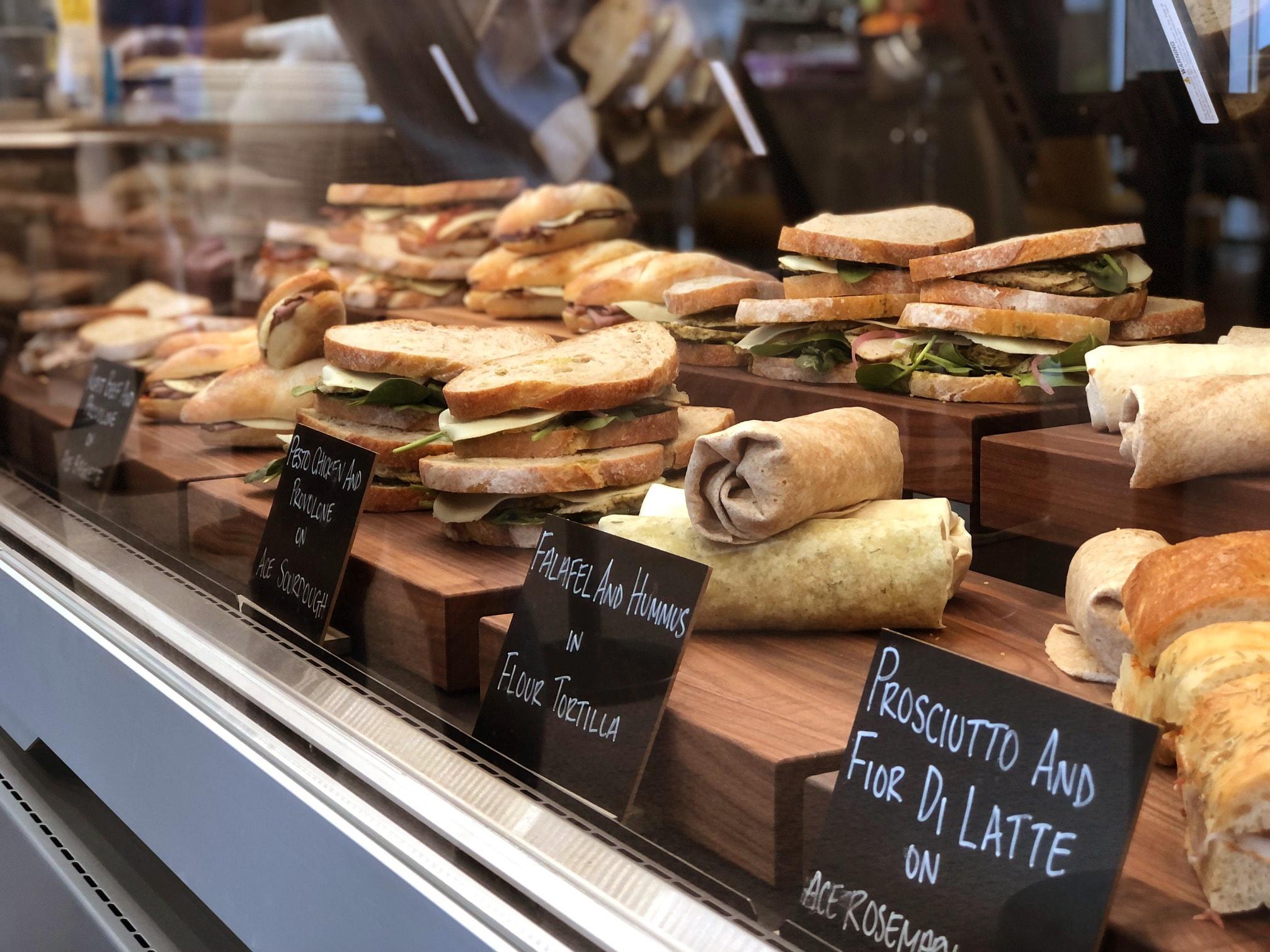 Delicious looking deli wraps and sandwiches behind a cafeteria lunch counter at 1 President’s Choice Circle head office. Signs reading "prosciutto and fior de latte" and "falafel and hummus in flour tortilla".